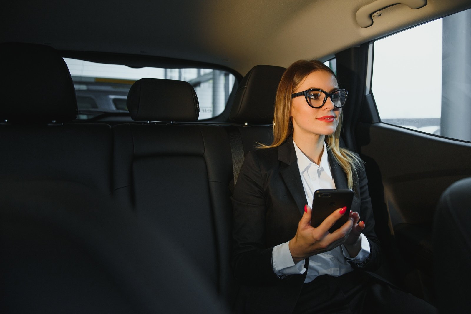 Smart businesswoman sits at backseat of the luxury car with black interior.