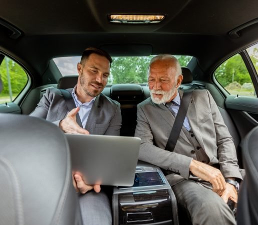 Business professionals discuss strategies on a laptop while traveling in a luxury car Small Group Luxury Sedan & SUV transportation