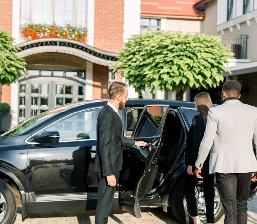 Chauffeur man opening car door for business couple, Caucasian woman and African man, side view